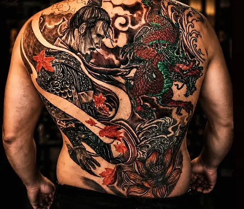 Costas inteiras tatuadas com um samurai de armadura, um dragão vermelho e verde, ondas, folhas de bordo vermelhas e uma flor de lótus